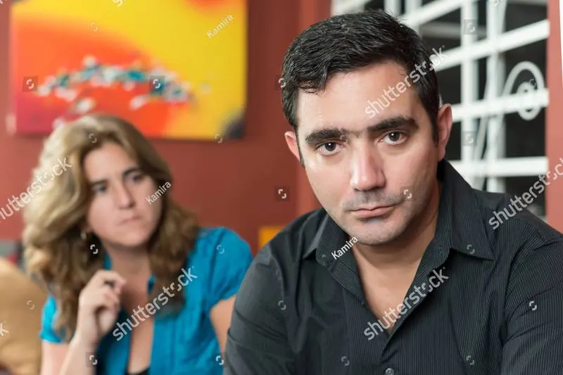A man in the foreground looking at the camera with a woman out of focus behind him