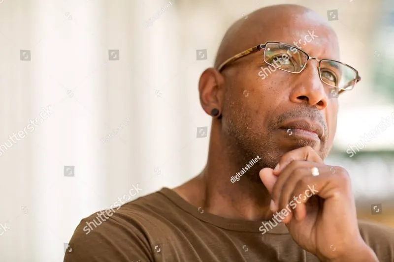 A man with glasses resting his hand at his chin, looking past the camera